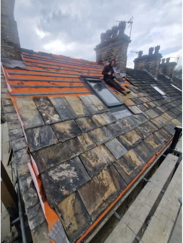Reclaimed stone slates being re-laid around a Velux window mid re-roof